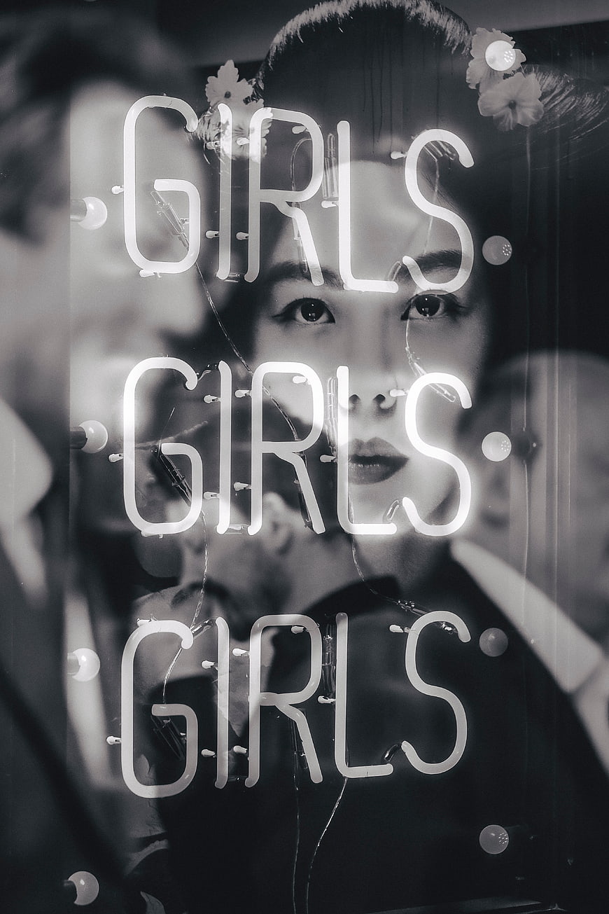 Black and white woman behind neon girls sign