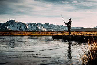 Man fly fishing in river with snow-capped mountains