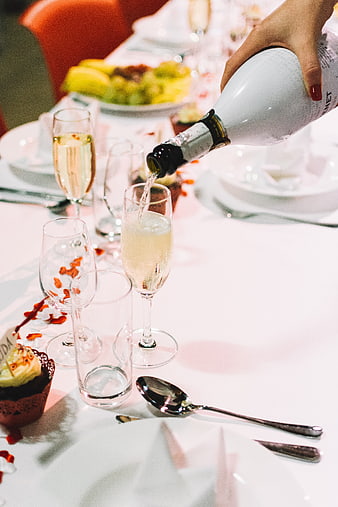 Hand pouring champagne into a glass at a wedding reception table