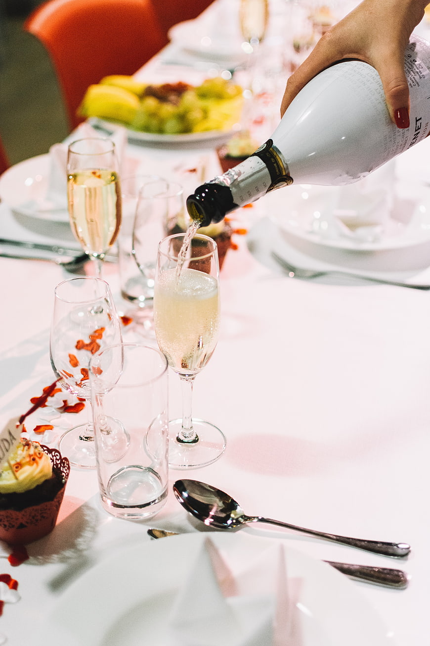 Hand pouring champagne into a glass at a wedding reception table