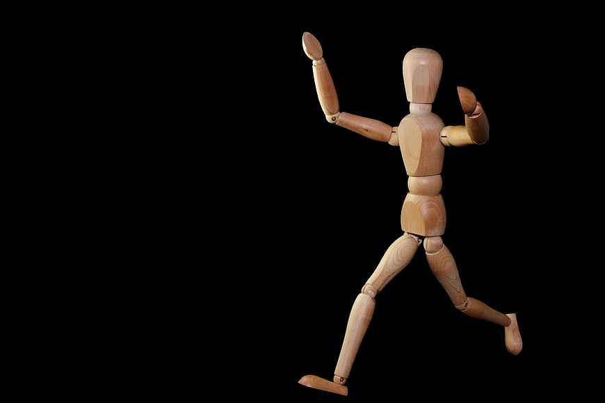 Wooden artist mannequin running pose on black background