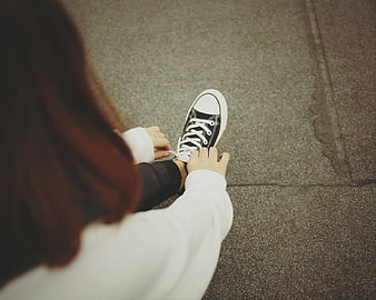 Woman tying black and white sneakers on pavement