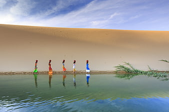 Women in colorful traditional dresses walking by a lake near sand dunes
