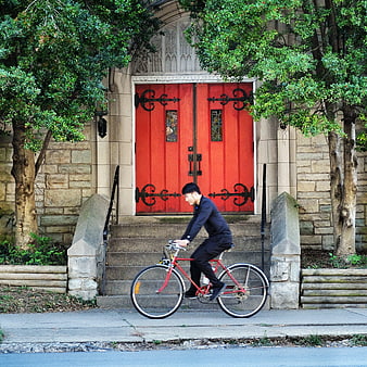 Man cycling past historic red church doors