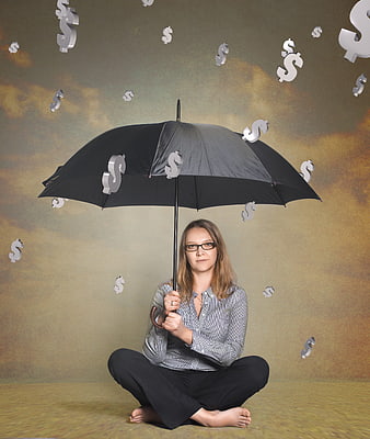 Woman holding umbrella against falling dollar signs