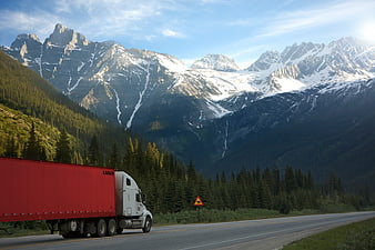 Red semi-truck driving on highway with snowy mountains