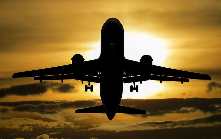 Silhouette of Airplane Landing Against Golden Sunset Sky