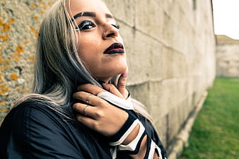Gothic woman with dark makeup and nose ring against stone wall