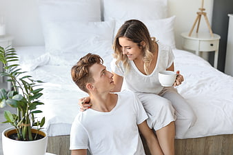 Happy young couple relaxing in bright white bedroom with coffee