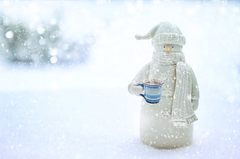 Cute ceramic snowman figurine holding blue mug in snowy winter scene