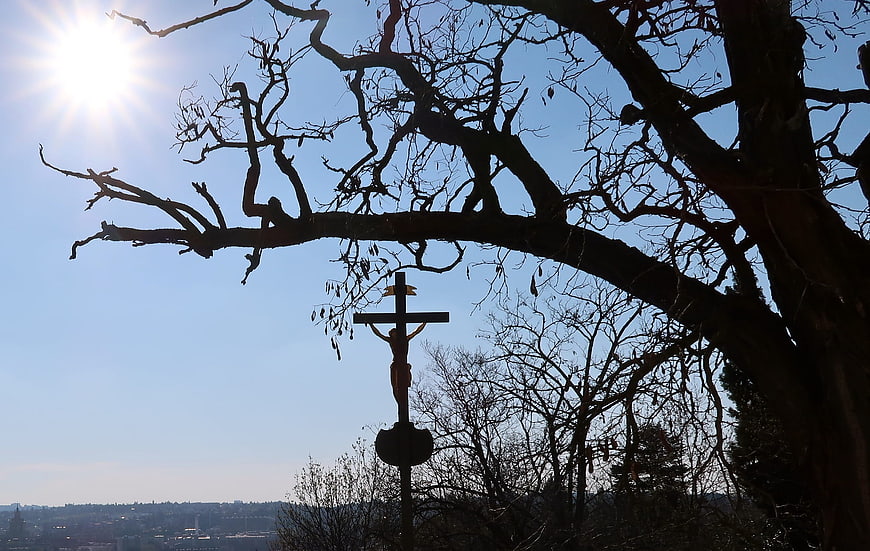 Silhouette of crucifix under bare tree branches against blue sky