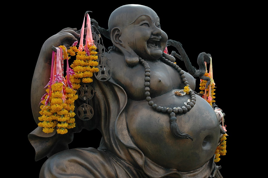Laughing Buddha Statue with Marigold Garlands on Black Background