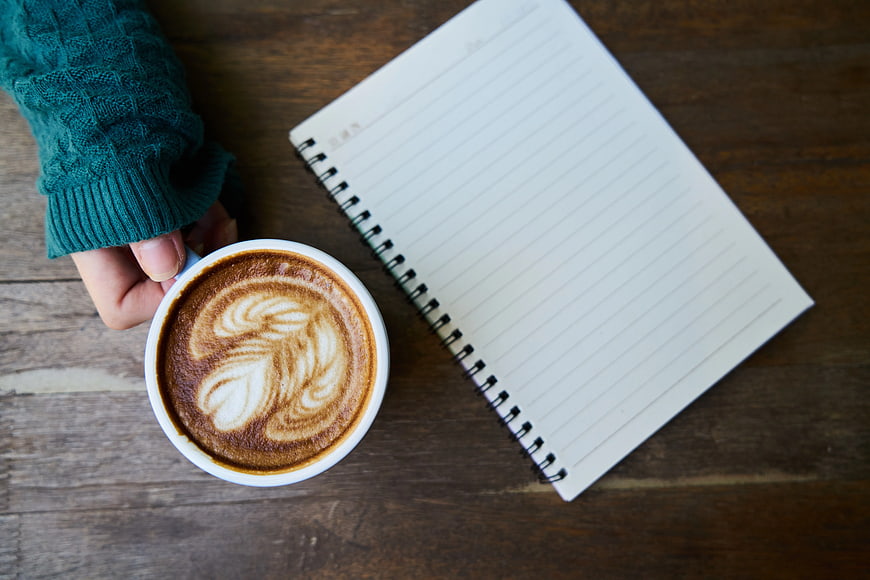 Flat lay of cappuccino with latte art and notebook on wood