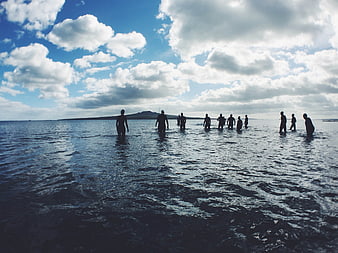 Silhouettes of people standing in ocean water under cloudy sky