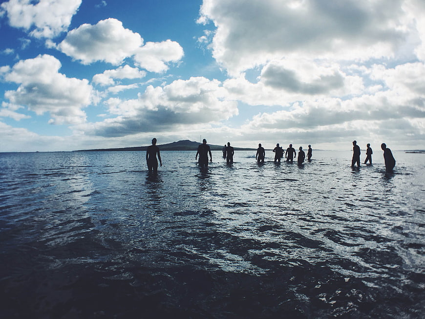 Silhouettes of people standing in ocean water under cloudy sky