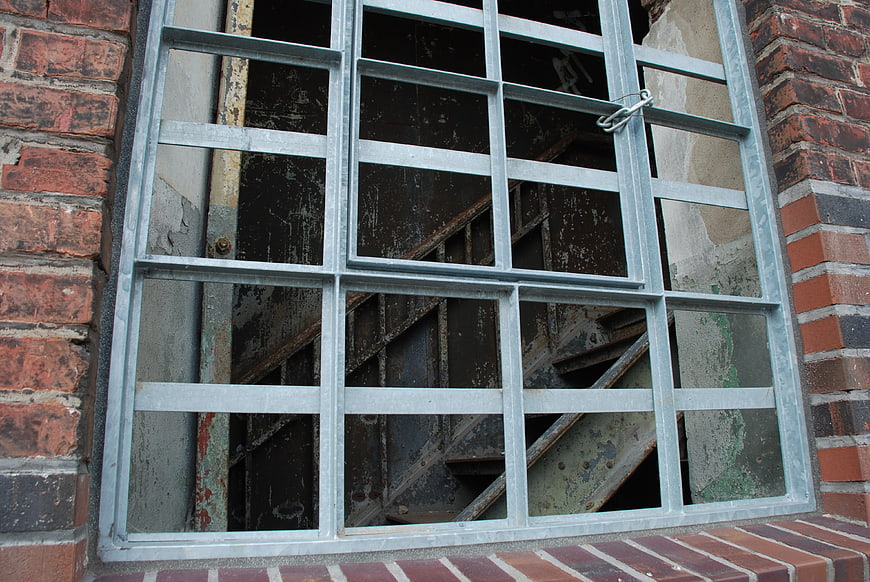 Rusty metal staircase behind barred window in old brick factory