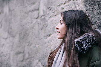 Profile of smiling woman in winter coat against stone wall