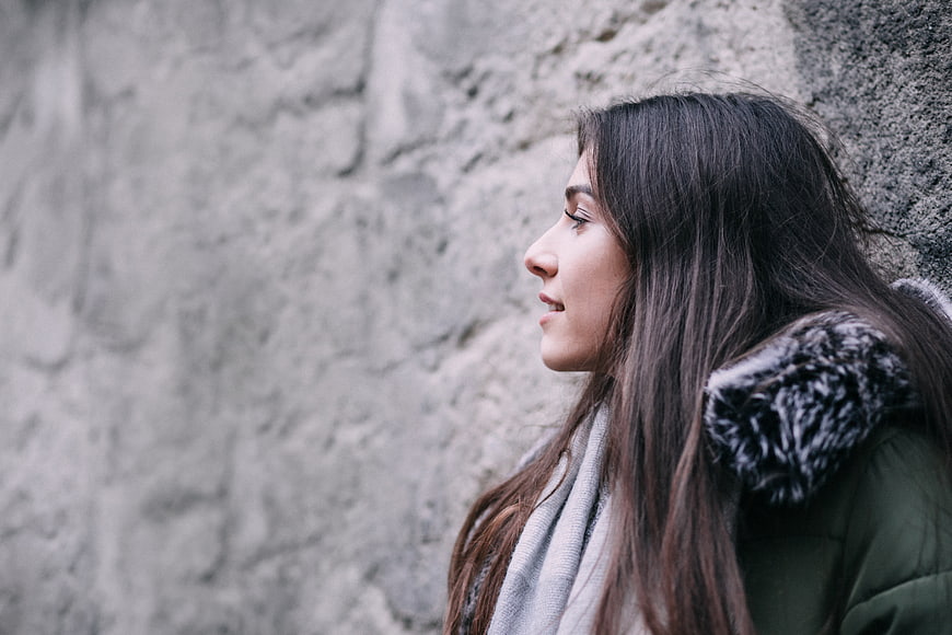 Profile of smiling woman in winter coat against stone wall