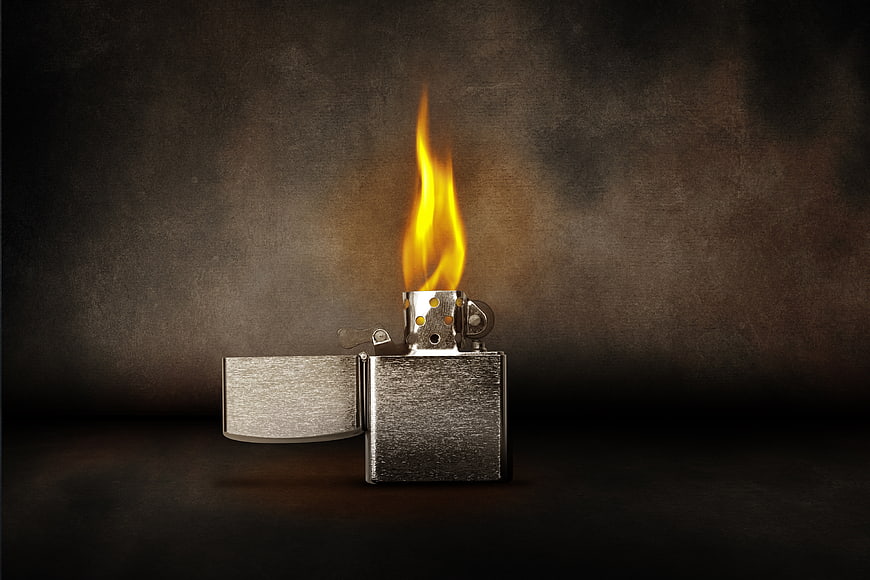 Lit silver lighter with bright flame on dark textured background