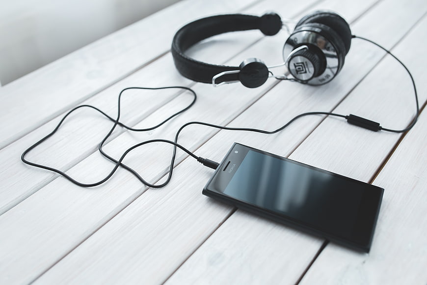 Black Smartphone and Headphones on White Wooden Table