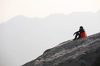 Man sitting on rocky mountain peak overlooking misty valley