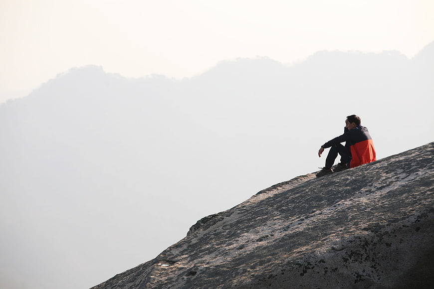 Man sitting on rocky mountain peak overlooking misty valley