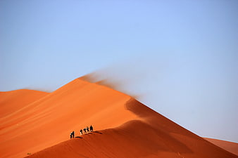 Hikers on Orange Sand Dunes in Desert Landscape