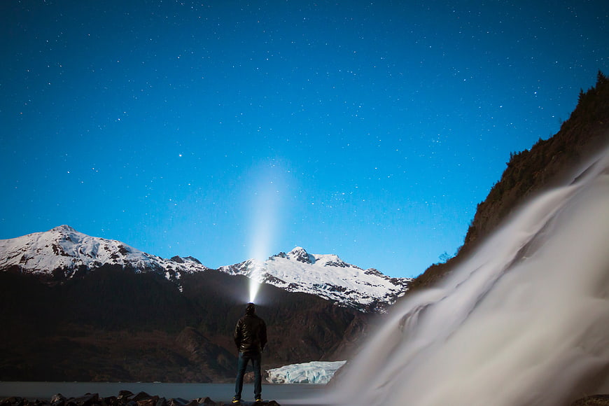 Man with Flashlight Beam Under Starry Night Sky