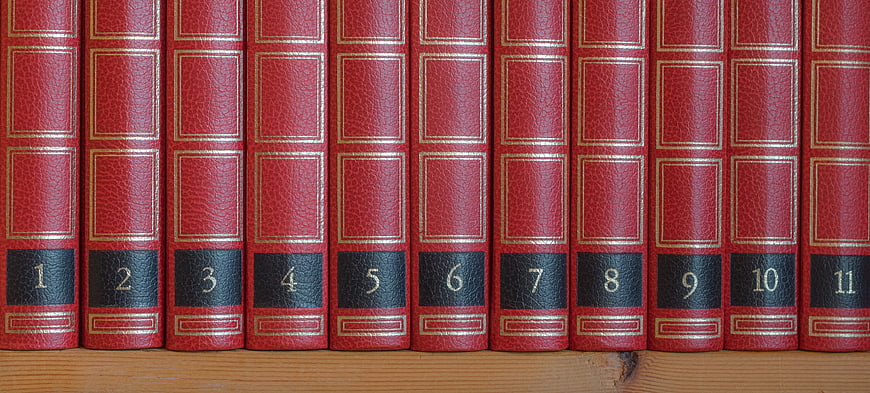 Row of red leather-bound books numbered 1 to 11 on a wooden shelf
