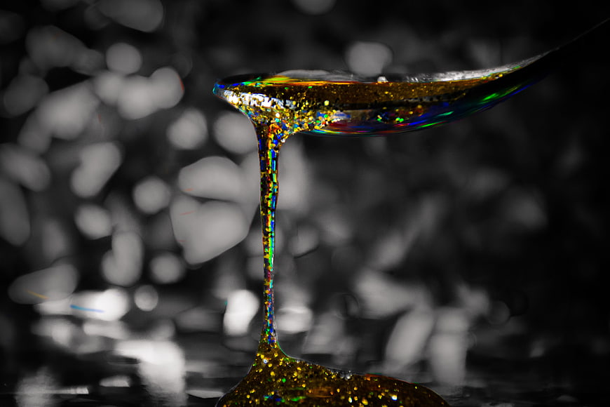 Golden Glitter Honey Dripping from Spoon on Dark Background