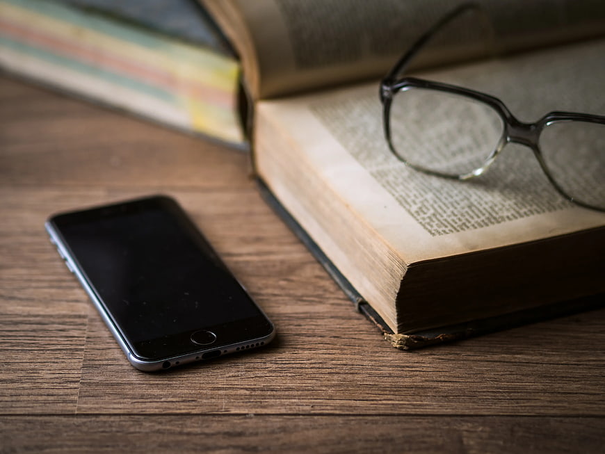 Smartphone and Open Book with Glasses on Wooden Table