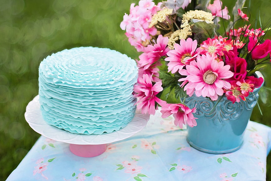 Blue ruffled cake with pink flowers on floral tablecloth