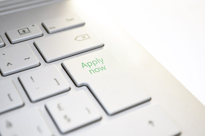 Close-up of white laptop keyboard with green apply now text