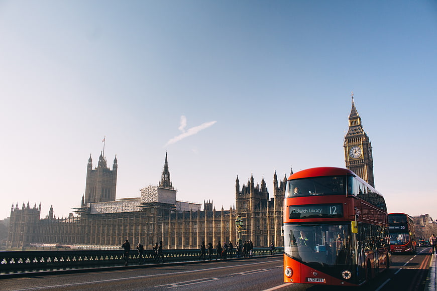 Red double-decker bus driving past Big Ben and Houses of Parliament in London
