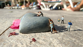 Miniature workers repairing a heart-shaped stone on a sunny pavement