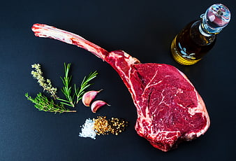 Raw Tomahawk Steak With Herbs, Garlic, Spices, And Olive Oil On Dark Background