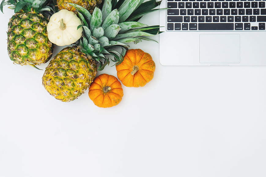 Flat lay of pineapples, pumpkins, and laptop on white background