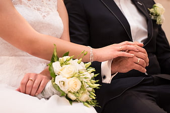 Close-up of wedding couple holding hands with rings and white bouquet