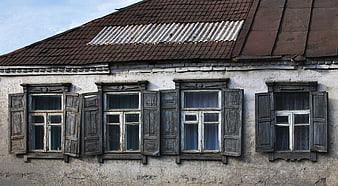 Old rustic house facade with weathered wooden windows and shutters