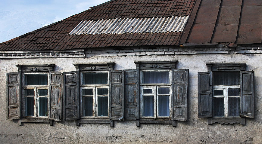 Old rustic house facade with weathered wooden windows and shutters