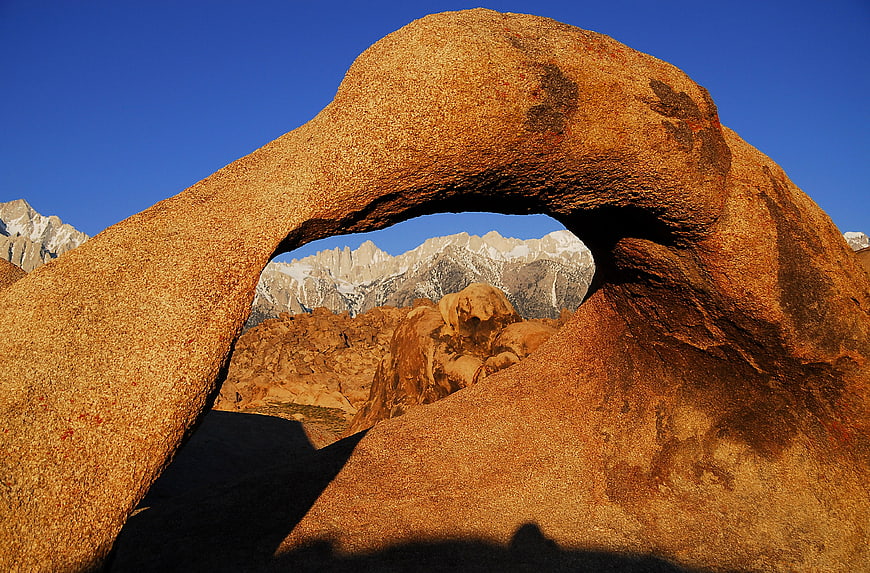 Natural Rock Arch Framing Snowy Mountain Peaks at Sunrise