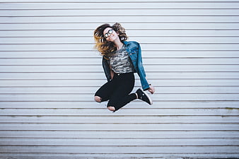 Young woman jumping in front of white slatted wall