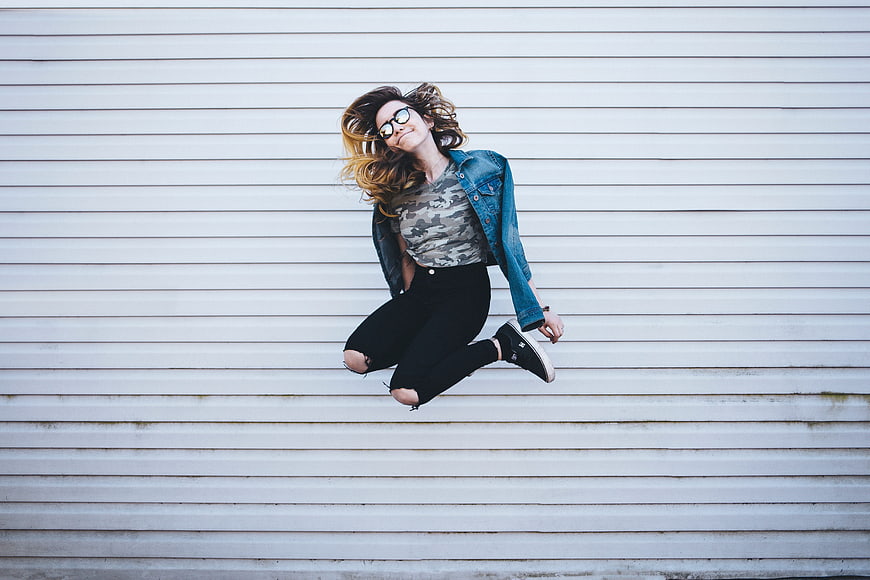 Young woman jumping in front of white slatted wall