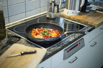 Shakshuka with peppers and eggs cooking in a frying pan on a kitchen stove