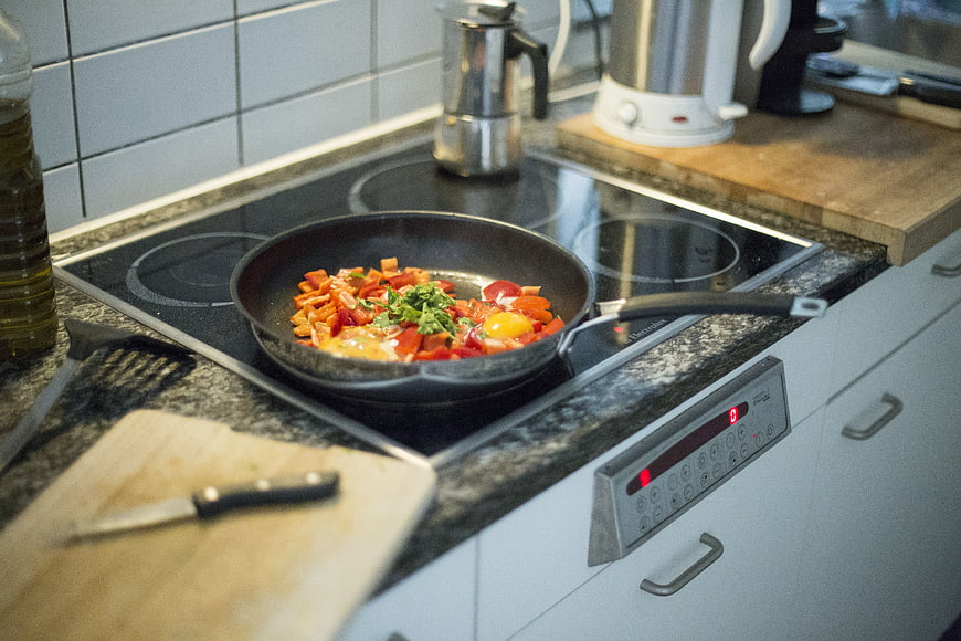 Shakshuka with peppers and eggs cooking in a frying pan on a kitchen stove
