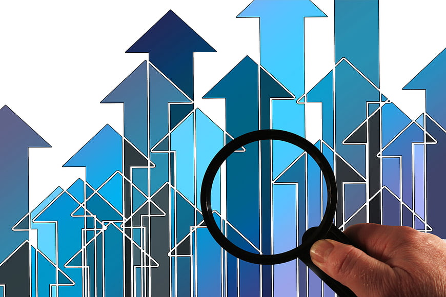 Hand holding magnifying glass over blue growth arrows
