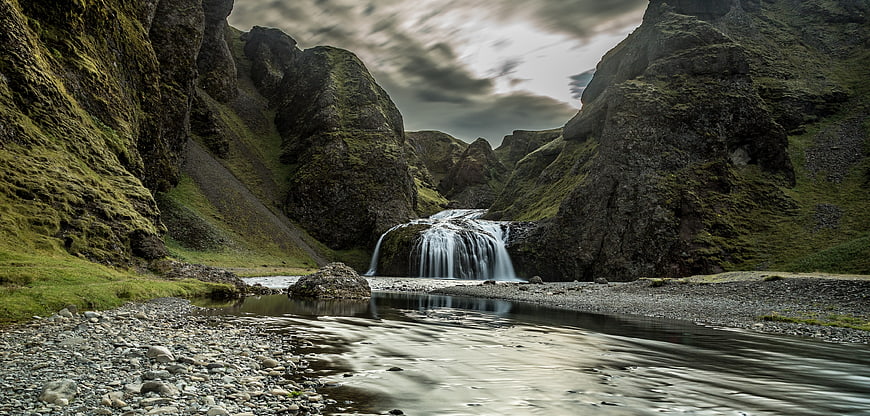 Dramatic waterfall in mossy Icelandic canyon with long exposure river