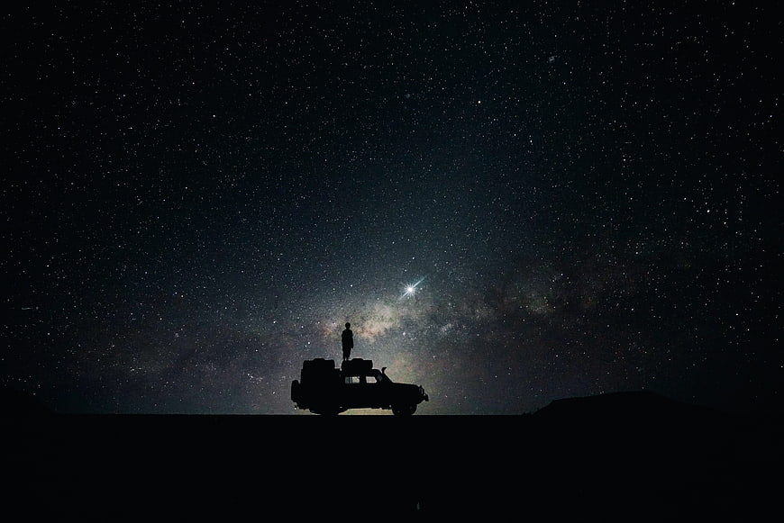 Silhouette of Man Standing on Car Roof Under Starry Night Sky