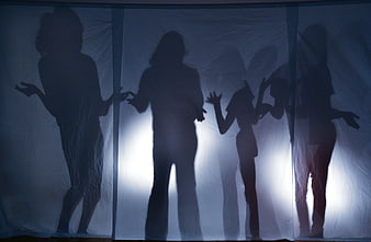 Silhouettes of women standing behind a translucent blue fabric
