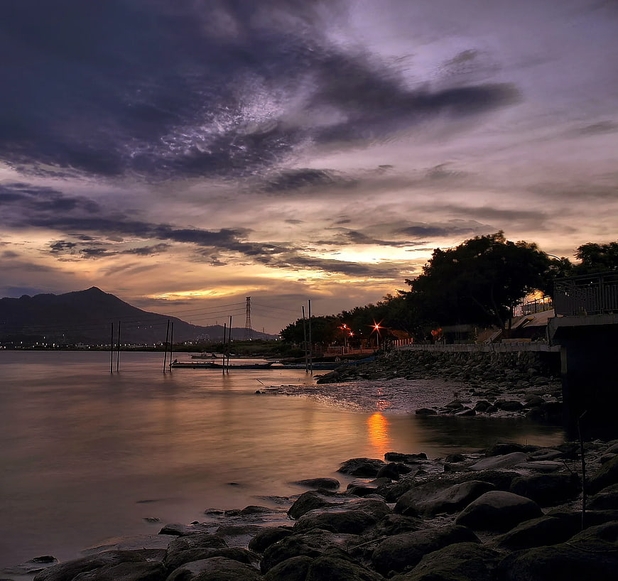 Dramatic sunset over rocky shoreline with smooth water